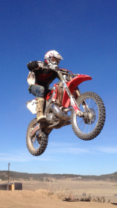 Logan Bryson in the air as he is jumping a table top at Palmer Lake dirtbike track.