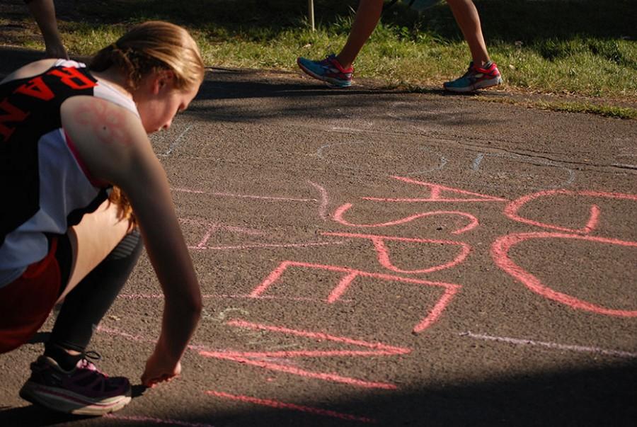 Rebekka Olson, 10, chalks the course at Heritage High School to show her team support.