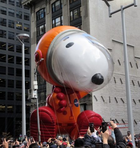 Astronaut Snoopy, designed by Joey Ammons, flies above the crowd as spectators photograph and record the beloved beagle character. 2019 Macys 93rd Thanksgiving Day Parade Astro Snoopy 0551A by Brechtbug is licensed with CC BY-NC-ND 2.0. To view a copy of this license, visit https://creativecommons.org/licenses/by-nc-nd/2.0/