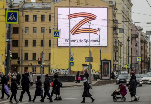People+crossing+under+a+billboard+featuring+a+%E2%80%98Z%E2%80%99%2C+the+symbol+of+the+Russian+and+Ukrainian+war.+The+text+below+the+%E2%80%98Z%E2%80%99+reads%3A+%E2%80%9CWe+don%E2%80%99t+give+up+on+our+people.%E2%80%9D+